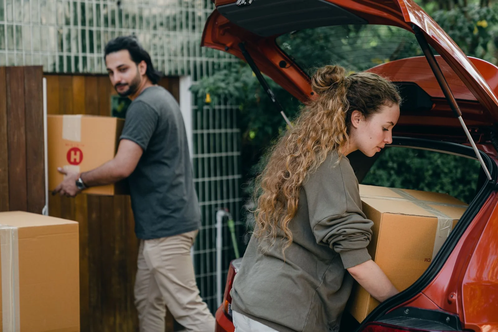 Paar lädt Umzugskartons aus dem Auto im grünen Außenbereich eines Hauses