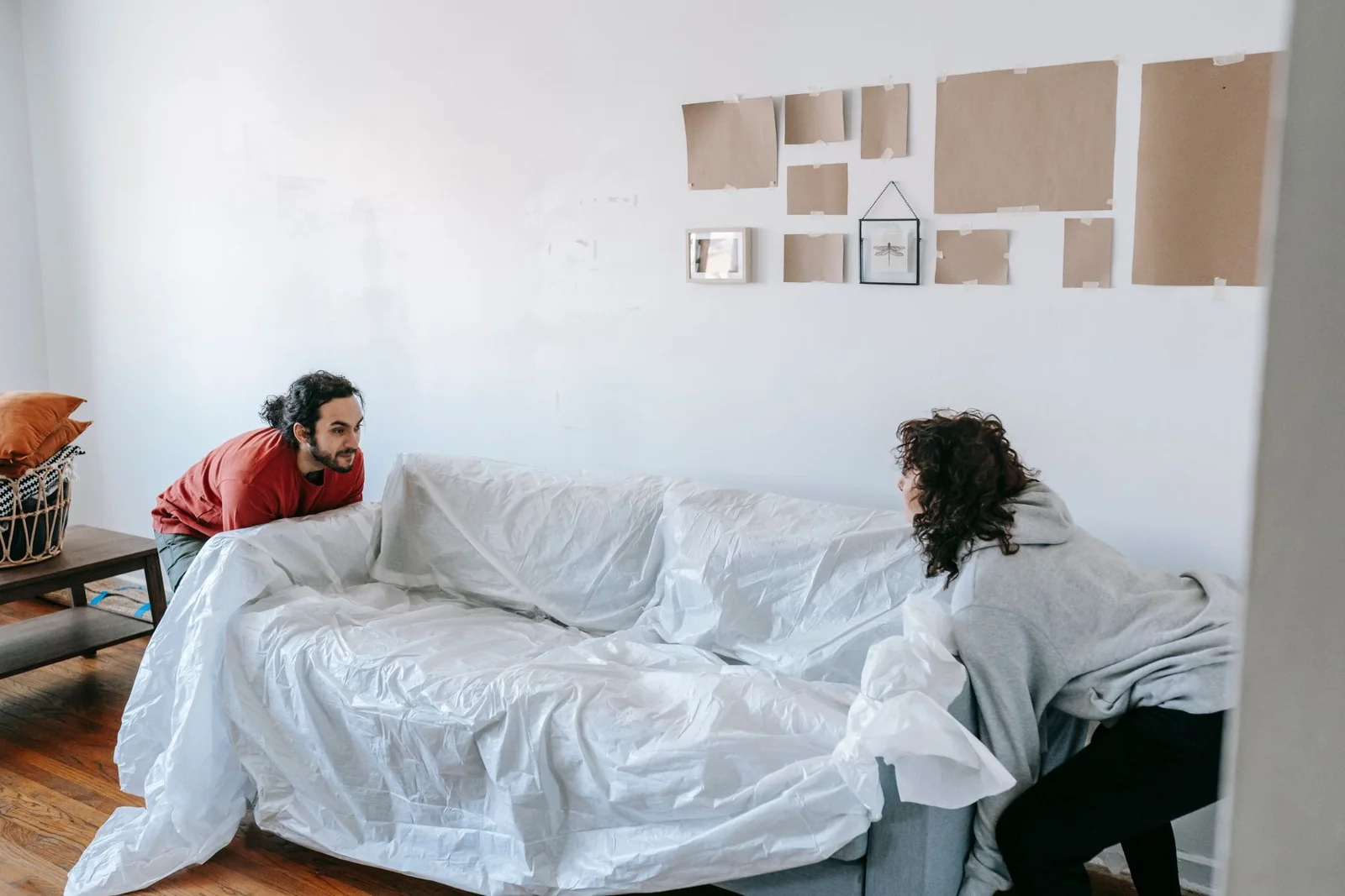 Zwei Personen heben gemeinsam ein mit Schutzfolie abgedecktes Sofa