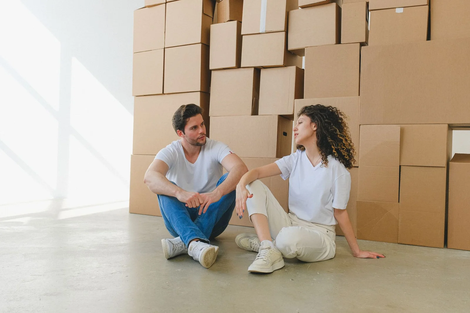 Paar sitzt im Gespräch vor gestapelten Umzugskartons in einer hellen Wohnung